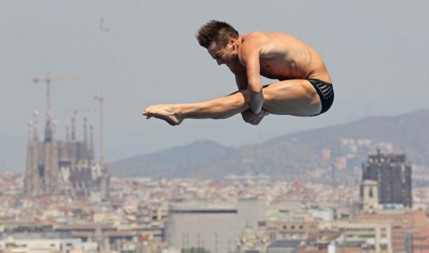 Ein Turmspringer in der Luft vor der Skyline von Barcelona.