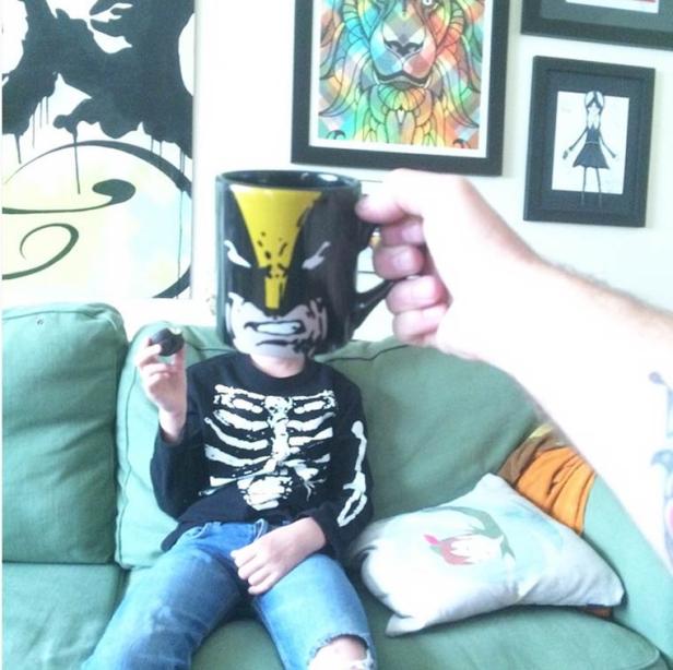 Ein Kind mit Skelett-Shirt hält eine Tasse mit Wolverine-Motiv vor sein Gesicht.