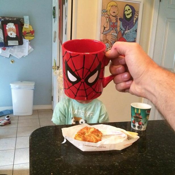 Ein Kind sitzt am Tisch, während eine Spiderman-Tasse vor sein Gesicht gehalten wird.