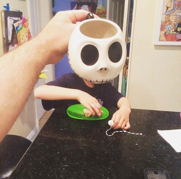 Ein Kind isst, während eine Jack Skellington Tasse vor sein Gesicht gehalten wird.