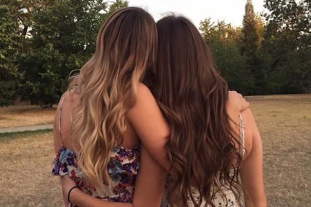 Zwei junge Frauen umarmen sich im Freien, ihre Rücken sind dem Betrachter zugewandt.