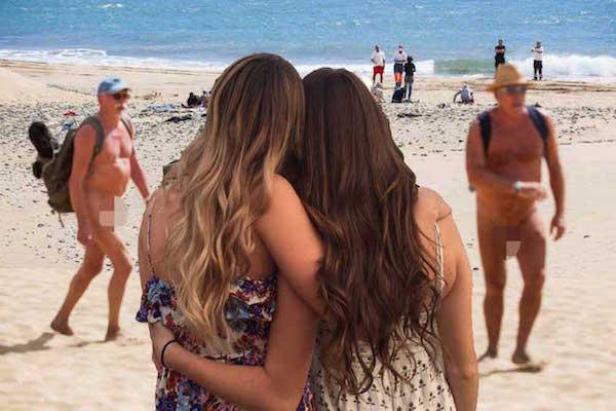 Zwei Frauen umarmen sich am Strand, während im Hintergrund unbekleidete Menschen zu sehen sind.