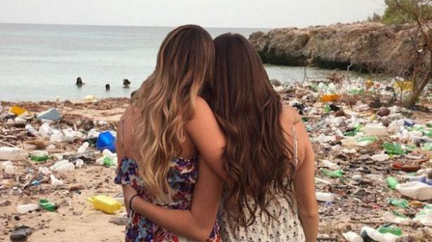 Zwei Frauen stehen an einem Strand voller Müll.