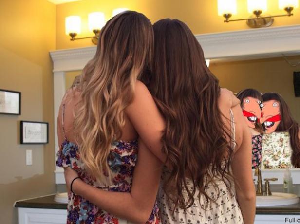 Zwei junge Frauen umarmen sich vor einem Spiegel im Badezimmer.