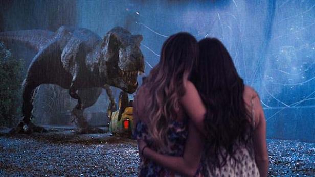 Zwei Frauen umarmen sich vor einem Tyrannosaurus Rex im Regen.