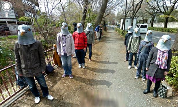 Eine Gruppe von Menschen mit Taubenkopfmasken steht am Straßenrand.