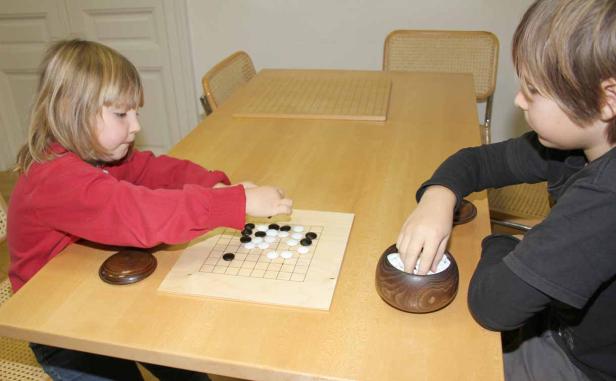 Zwei Kinder spielen das Brettspiel Go an einem Tisch.