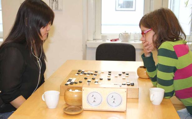 Zwei Frauen spielen Go an einem Tisch mit einer Go-Uhr.