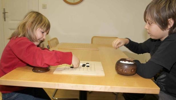 Zwei Kinder spielen das Brettspiel Go an einem Tisch.