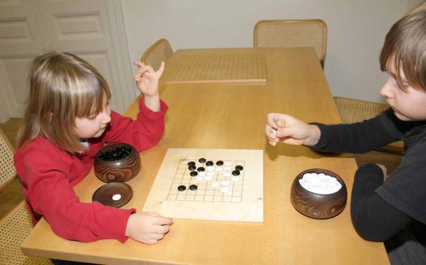Zwei Kinder spielen das Brettspiel Go an einem Tisch.