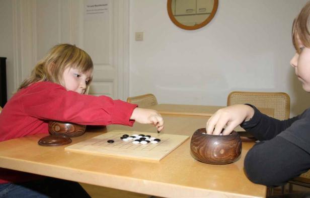 Zwei Kinder spielen das Brettspiel Go an einem Tisch.