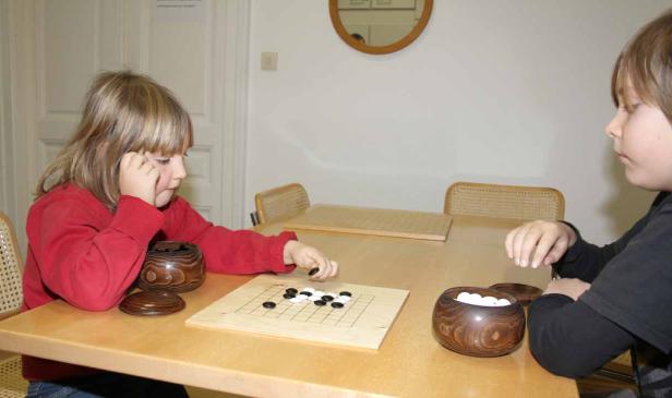 Zwei Kinder spielen das Brettspiel Go an einem Tisch.