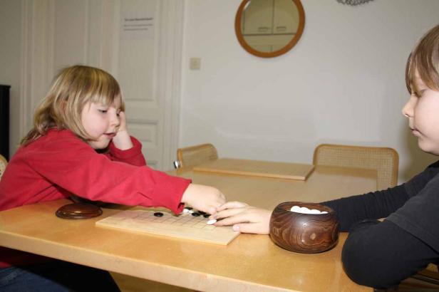 Zwei Kinder spielen das Brettspiel Go an einem Tisch.