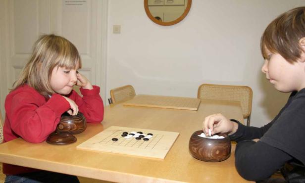 Zwei Kinder spielen das Brettspiel Go an einem Tisch.