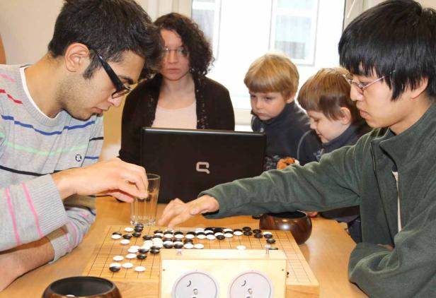 Zwei Männer spielen Go, während eine Frau und zwei Kinder zusehen.