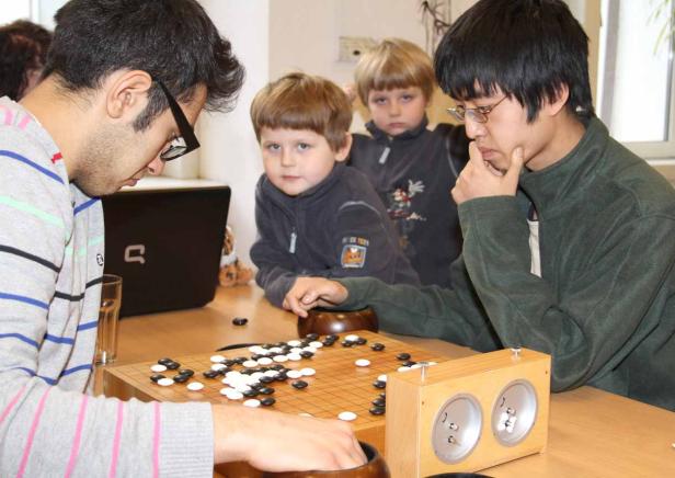 Zwei Männer und zwei Kinder spielen Go an einem Tisch.