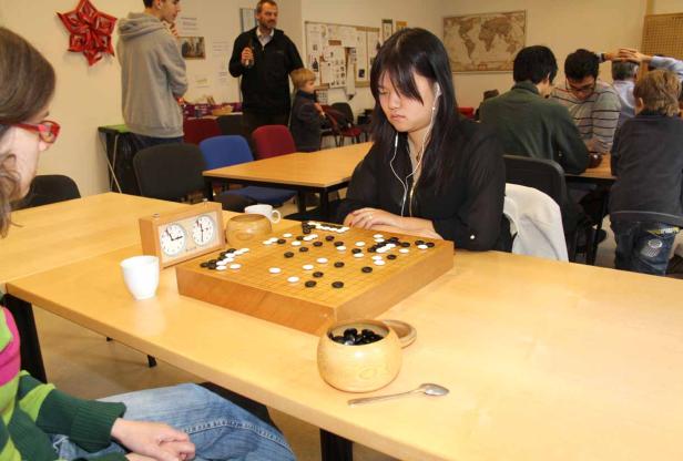 Eine junge Frau spielt das Brettspiel Go mit einer Spieluhr auf dem Tisch.