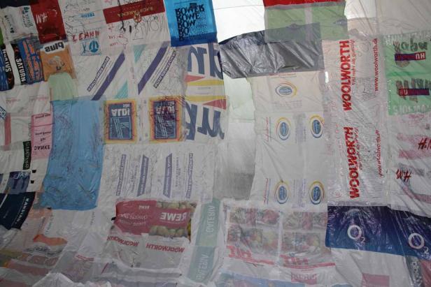 Eine Wand bedeckt mit verschiedenen Plastiktüten von Geschäften wie Woolworth und Saturn.