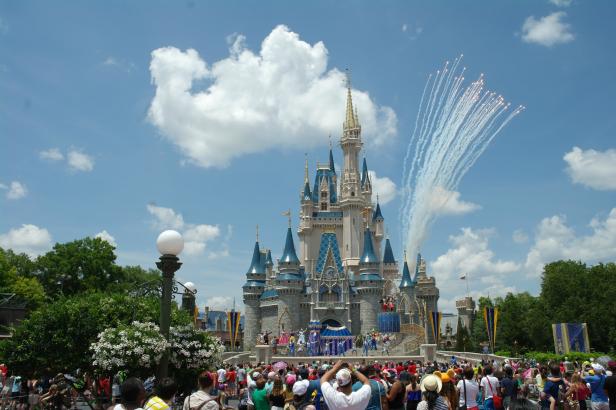 Besucher beobachten eine Bühnenshow vor dem Cinderella-Schloss im Magic Kingdom mit Feuerwerk im Hintergrund.