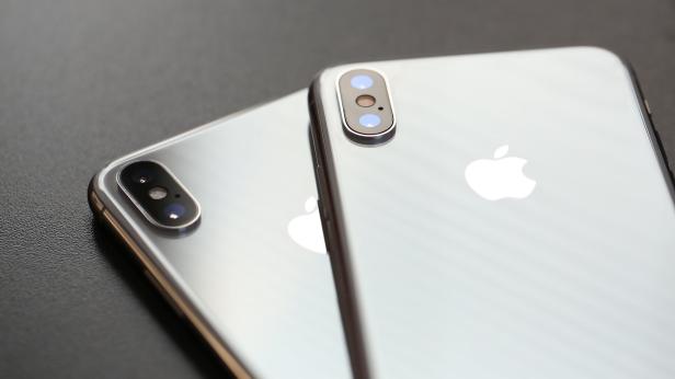 Zwei silberne iPhones liegen auf einer dunklen Oberfläche.