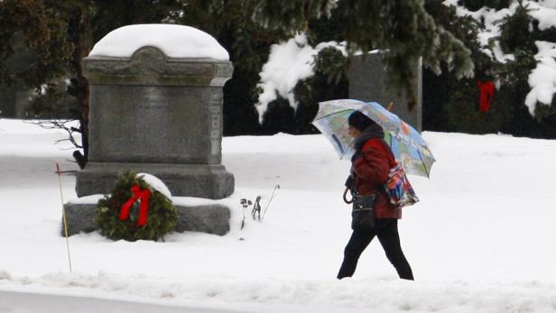 Eine Frau mit Regenschirm geht über einen verschneiten Friedhof.