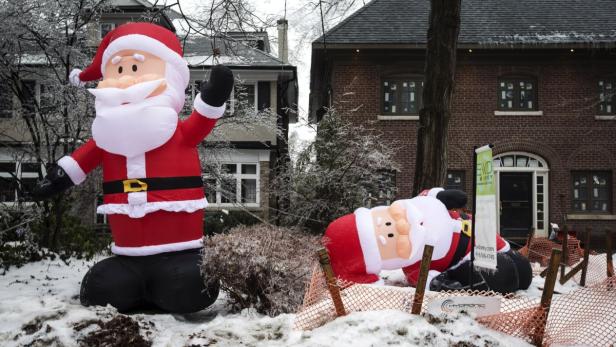 Zwei aufblasbare Weihnachtsmänner stehen vor Wohnhäusern im Schnee.
