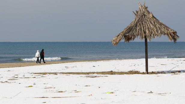 Ein schneebedeckter Strand mit einem Strohschirm und zwei Personen im Hintergrund.