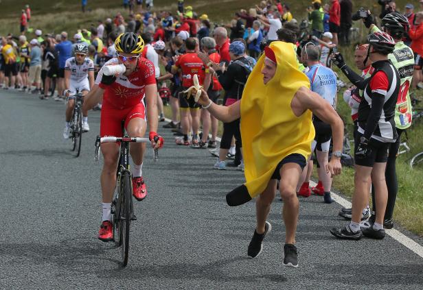 Ein Radfahrer trinkt, während ein Mann im Bananenkostüm ihm eine Banane reicht.