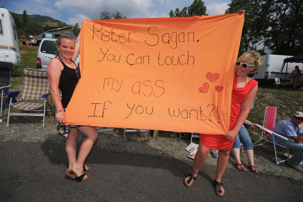 Zwei Frauen halten ein orangefarbenes Transparent mit der Aufschrift „Peter Sagan, You Can touch my ASS If You want?!“.