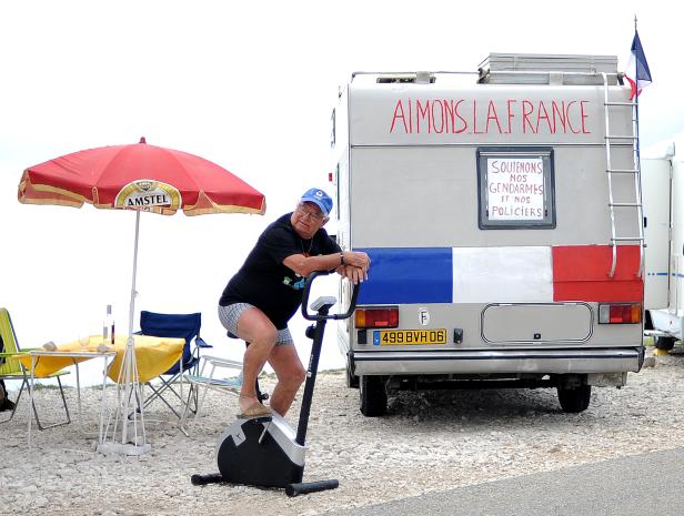 Ein Mann „radelt“ vor einem Wohnwagen mit der Aufschrift „Aimons la France“.