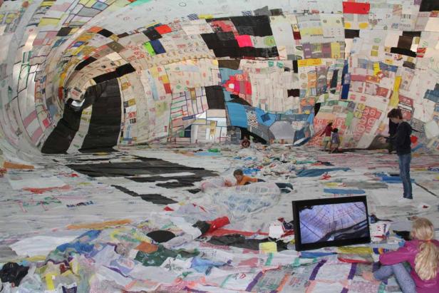 Kinder spielen in einer tunnelartigen Installation aus recycelten Plastiktüten.