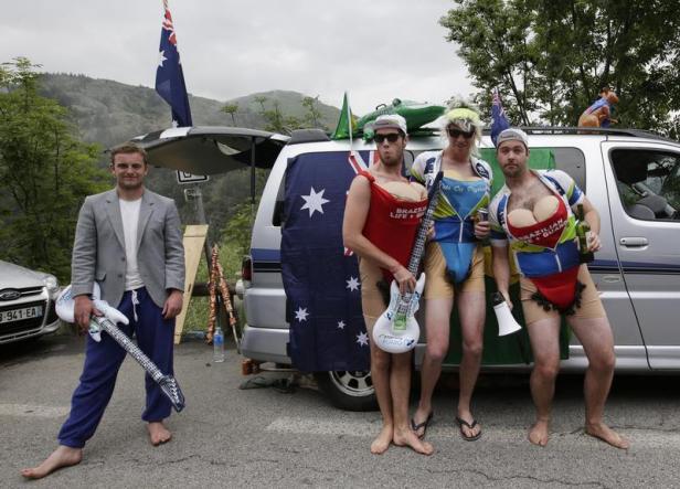 Eine Gruppe von Männern posiert mit australischen Flaggen und skurrilen Kostümen vor einem Auto.