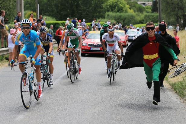 Radrennfahrer fahren ein Rennen, während ein als Robin verkleideter Mann mitläuft.