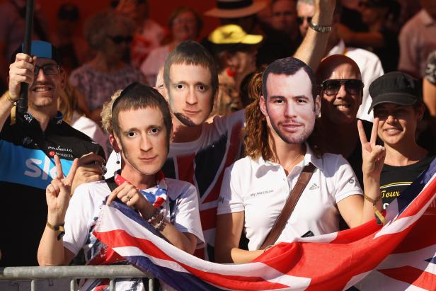 Radrenn-Fans schwenken die britische Flagge und halten Masken von Radrennfahrern hoch.