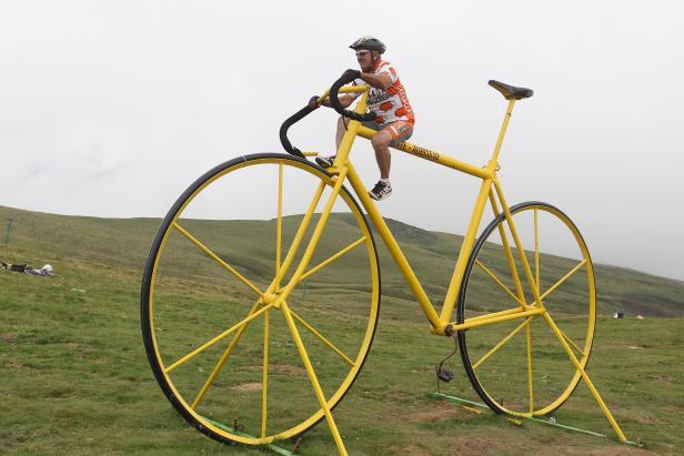 Ein Mann sitzt auf einem riesigen gelben Fahrrad auf einer Wiese.