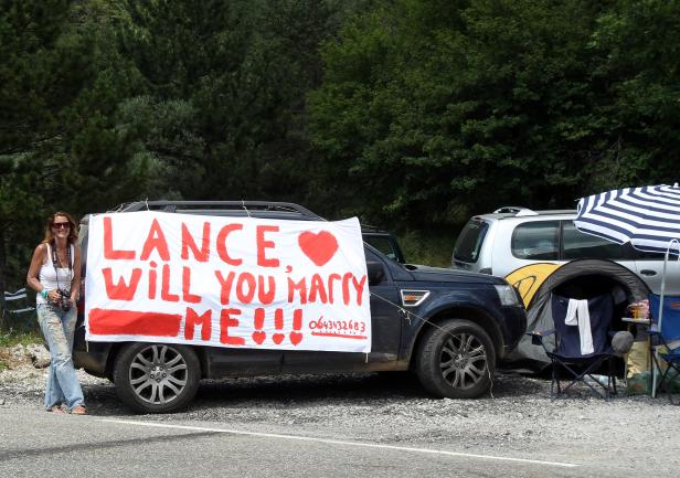 Eine Frau steht neben einem Auto mit einem handgemalten Heiratsantrag für Lance.