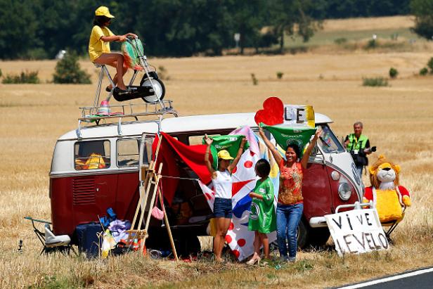 Eine Gruppe von Fans feuert die Tour de France von einem dekorierten VW-Bus aus an.