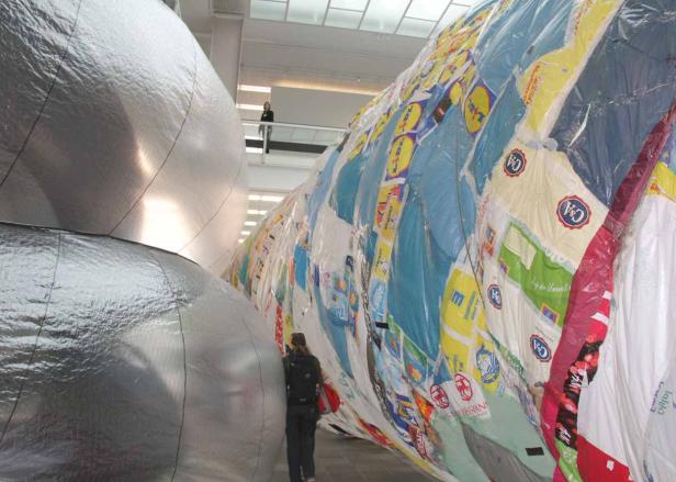 Eine Person steht vor einer großen Installation aus recycelten Einkaufstüten und silbernen Ballons.