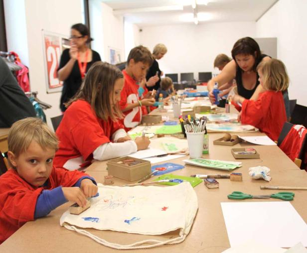Kinder sitzen an einem Tisch und bemalen Stoffbeutel und Papier.