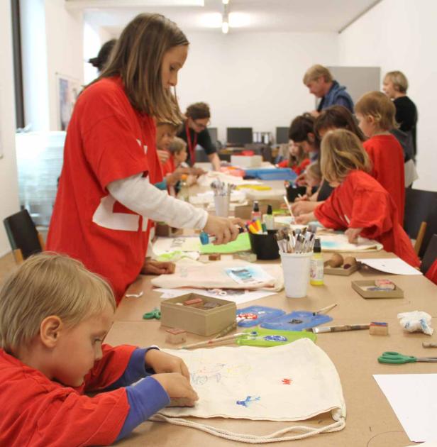 Kinder sitzen an einem Tisch und bemalen Stoffbeutel.