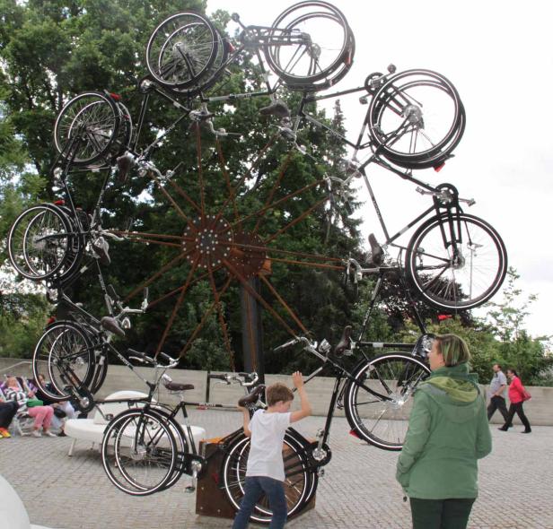 Ein Junge steht vor einem großen Rad, das aus Fahrrädern besteht.