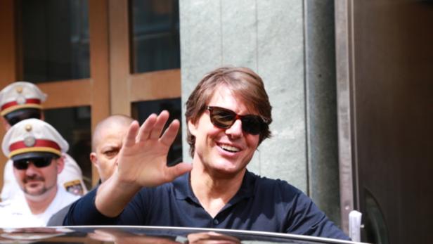 Tom Cruise lächelt und winkt in die Kamera.