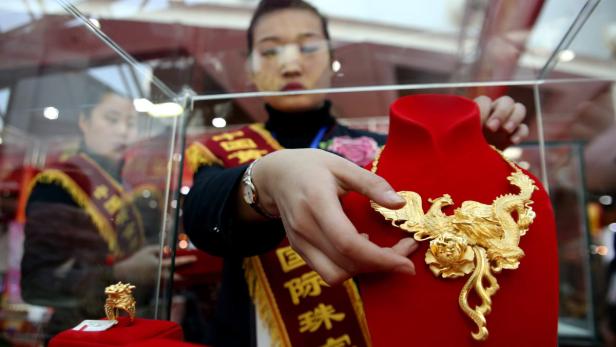 Eine Verkäuferin präsentiert eine goldene Halskette mit Drachen- und Phönixmotiven.