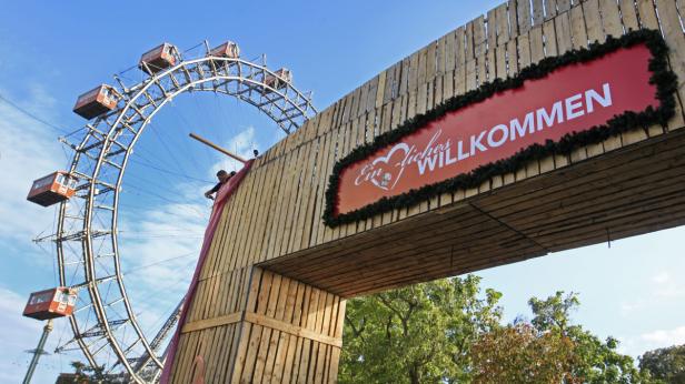 Das Wiener Riesenrad ist durch einen hölzernen Torbogen mit der Aufschrift „Ein herzliches Willkommen“ zu sehen.