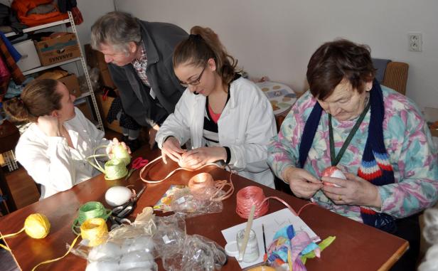 Eine Gruppe von Frauen und ein Mann sitzen an einem Tisch und basteln mit bunten Bändern.
