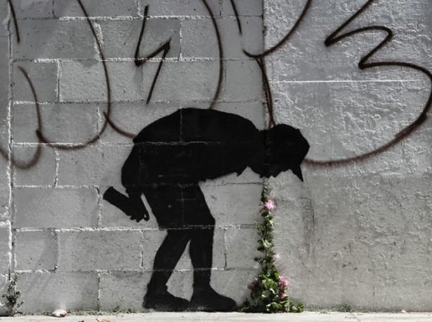 Ein Banksy-ähnliches Graffiti zeigt eine gebeugte Person, die eine Blume zu bewässern scheint.