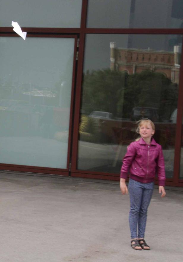 Ein Mädchen wirft ein Papierflugzeug vor einem modernen Gebäude.