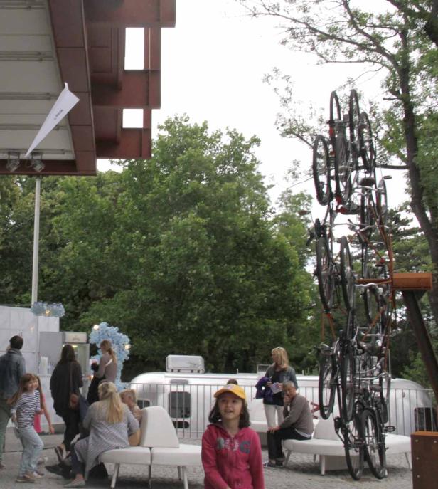 Eine Gruppe von Menschen versammelt sich vor einer Installation aus gestapelten Fahrrädern.