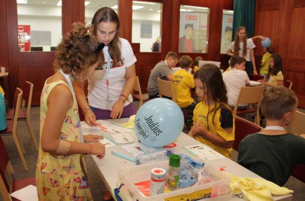 Kinder basteln mit einer Betreuerin in einem Raum mit dem Motto „Joulious entdeckt die Energie!“.