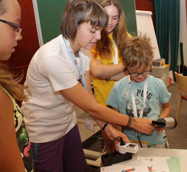 Ein Kind experimentiert mit einem Fön und einer Steckdose unter Aufsicht von Betreuern.